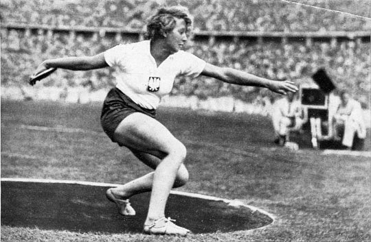 A German woman dicsus thrower competing in a stadium, at the 1936 Summer Olympics.
