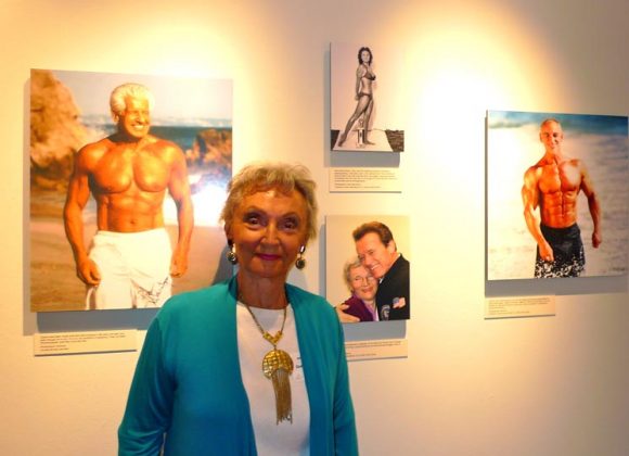 Bodybuilder Doris Barrilleaux at the 2011 Opening of the Joe and Betty Weider Museum of Physical Culture; a photograph of Barrilleaux posing and another of her with bodybuilder Arnold Schwarzenegger are two of the four photographs in the background.