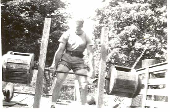 Weightlifter Bob Peoples using a wooden barbell, with a wooden power rack that Peoples invented.