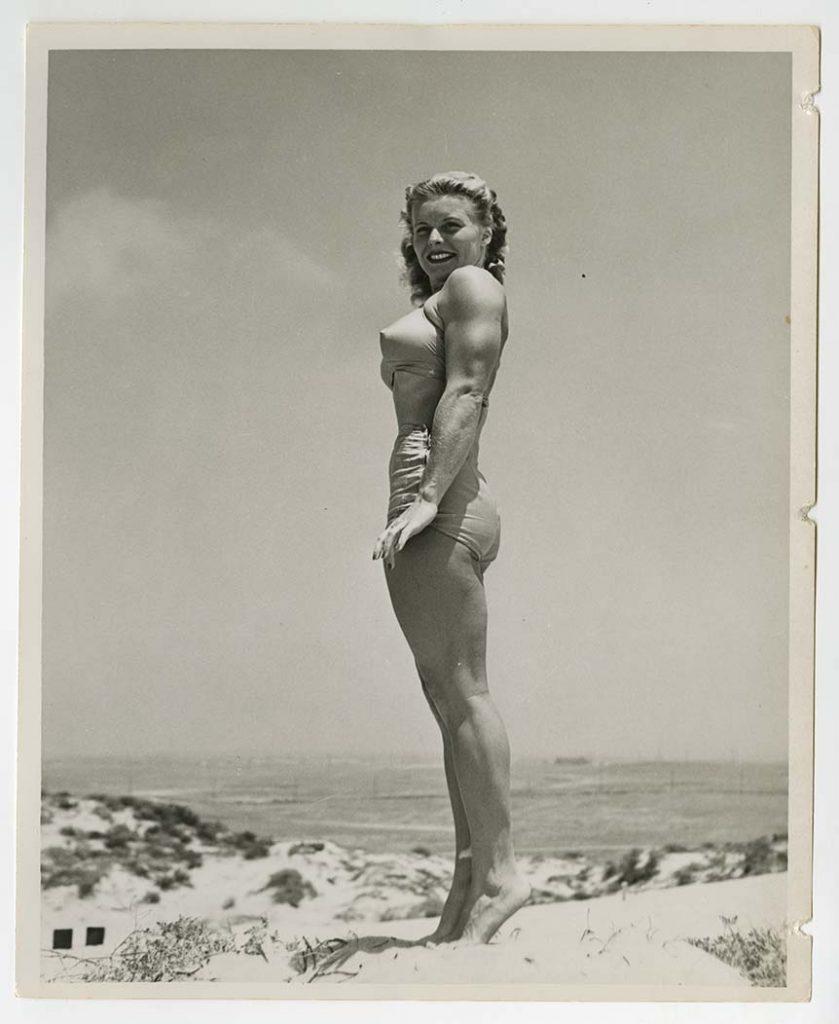 Bodybuilder Pudgy Stockton posing, in a bikini, on her tiptoes, on the beach, from the Pudgy and Les Stockton Collection.