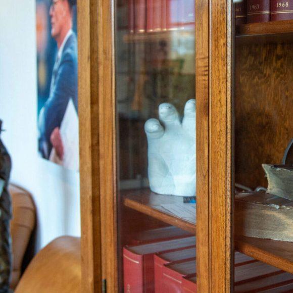 Physical culture items, including books and a plaster cast of a hand, in a display case, in the Reading Room; a statue and photograph of former Dallas Cowboys coach Tom Landry are in the background.