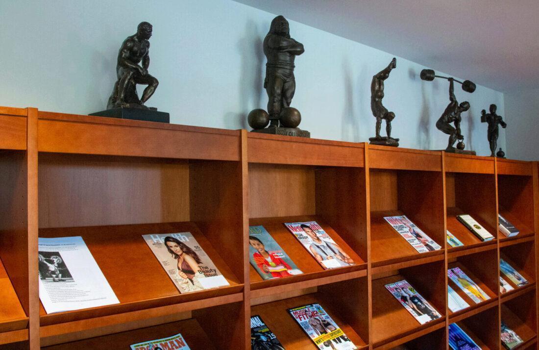 Five statues, including one of strongman Louis Cyr, and magazines on the open shelves of the library, in the Reading Room.