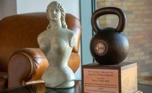 A sculpture of the bust of a woman, and Stark Center co-founder Terry Todd's kettlebell-shaped 2017 National Strength and Conditioning Association (NSCA) Alvin Roy Award for Career Achievement, in the Reading Room.