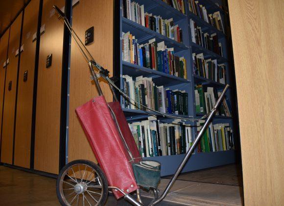A vintage red and green golf club cart with spoked wheels, donated by golf writer and historian Jim Apfelbaum, from the Jim Apfelbaum Collection, in the closed stacks room.