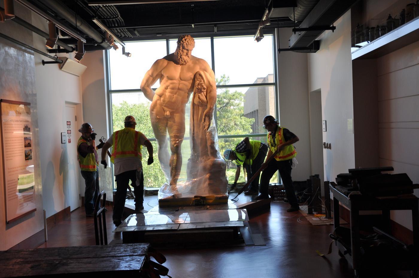 Front view of the statue of the Farnese Hercules wrapped and being moved, while four men work on it, in the main lobby.