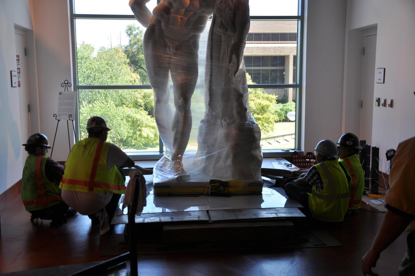 Front view of the bottom of the statue of the Farnese Hercules wrapped and being moved, while four men work on it, in the main lobby.
