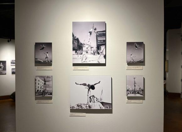 A photograph of one of the walls in the Muscle Beach exhibit. Black and white photos show various people performing acrobatic stunts.