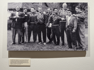 A photograph of a black and white photograph on display in the Strength & Friendship exhibit. In this photo, Bob Hoffman and the USA Weightlifting Team pose for a group photo.