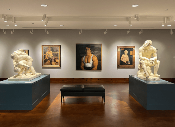 A photograph of the Teresa Lozano Long Fine Art Gallery shows two of the Battle casts (The Boxer and The Wrestlers) in the center of the room with original oil paintings of various weightlifters, strength athletes, and performers.