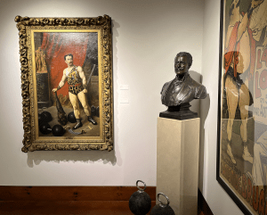 A photograph of the Professor Attila portrait, a bronze bust of Eugen Sandow, two of Professor Attila's kettlebells, and a portion of a promotional lithographic poster for La Loupiote.