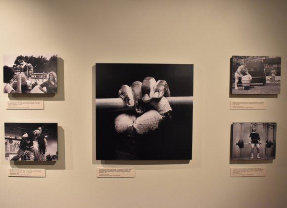 Five photographs of strong men and strong women, including a center one of wrestler and strongman Mark Henry's hand, and another of Stark Center co-founders Jan and Terry Todd (in the upper left), in the Strong Men, Strong Women Gallery.