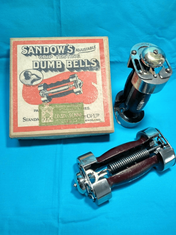 A box for two of strongman (Eugen) Sandow's Adjustable Grip Testing Dumb Bells and the two dumbbells, with one lying horizontally and the other standing vertically.