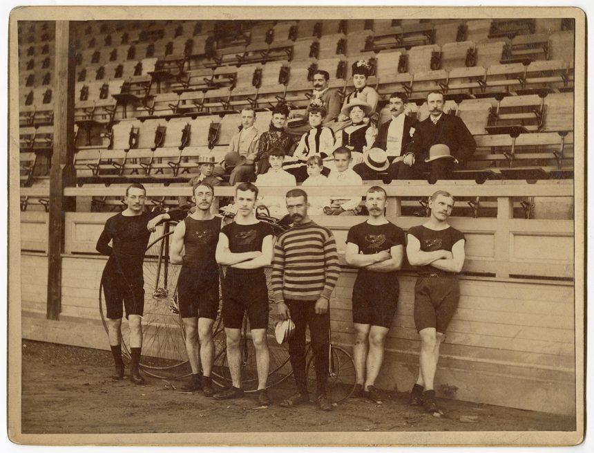 Six bicycle Racers at the Hartford (Connecticut) Wheel Club's bicycle tournament in Stamford, Connecticut, in 1889; twelve spectators are in the stands behind the racers.