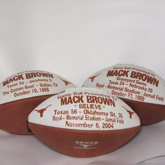 Three commemorative "Game Ball" footballs given to Mack Brown for the 1998 The Cotton Bowl, the 1999 Graveyard Game (Texas vs Nebraska), and the 2004 Texas vs Oklahoma game