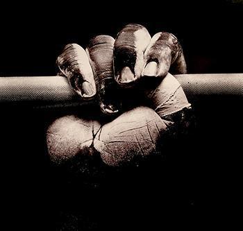 A black fist, dusted with chalk, tape on the thumb, grips a barbell, alluding to the gesture of black power and solidarity in the context of strength training and physical culture.