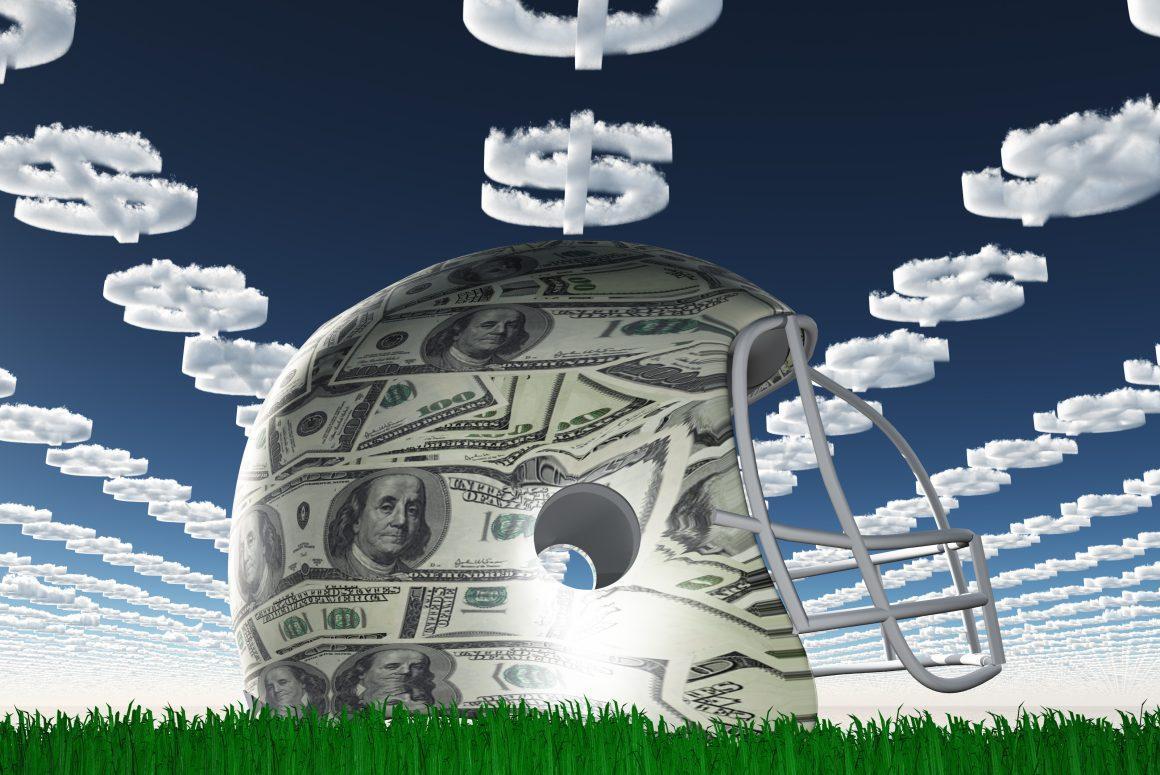 A football helmet overlayed with one hundred dollar bills sits on green grass with a blue sky overhead filled with money sign clouds
