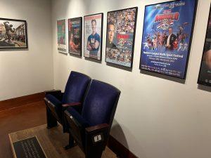 View of Arnold & Jim exhibit showing stadium chairs and on the wall various Arnold Classic posters.