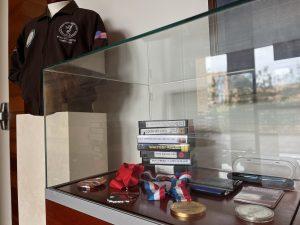 View Jim's leather jacket next to a display case with VHS tapes and medals at the entrance of Arnold & Jim exhibit.