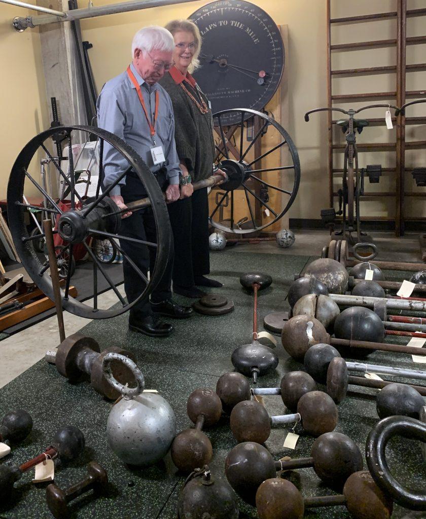 Walter Imahara and Stark Center Director Jan Todd deadlift the Mark Henry Wagon Wheel Barbell in the archives of The Stark Center.