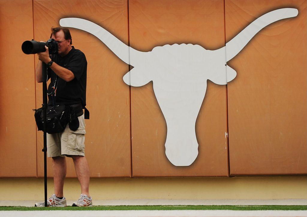 A color photo of Jim Sigmon behind a telephoto lens shooting a football game.