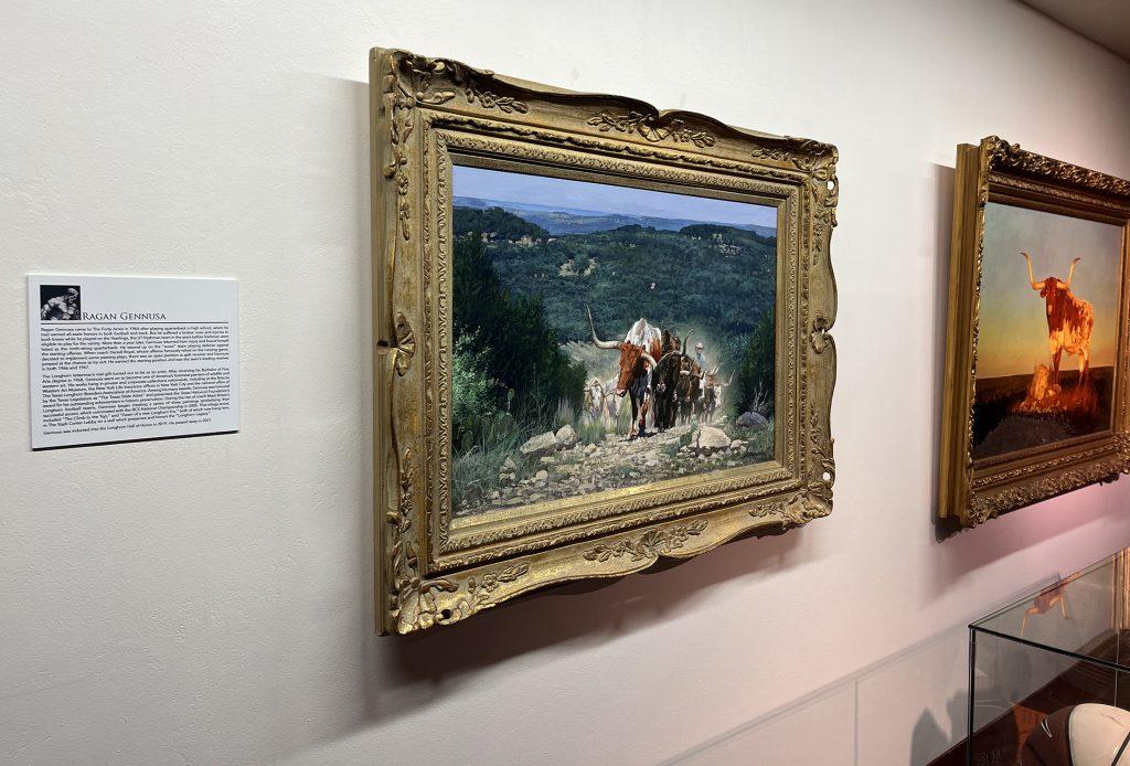 A white caption with black text in focus, next to two color oil paintings of longhorn cattle.