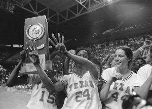 A photo of UT women's basketball players holding up the national championship trophy. One player shows 3-4 on their fingers to symbolize that their final record for the season was a perfect 34-0.