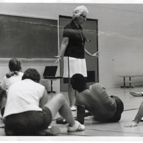 A photograph of Dr. Mary Evelyn Buice Alderson as she stands in front of a class seated on a gymnasium floor. She is teaching or lecturing.