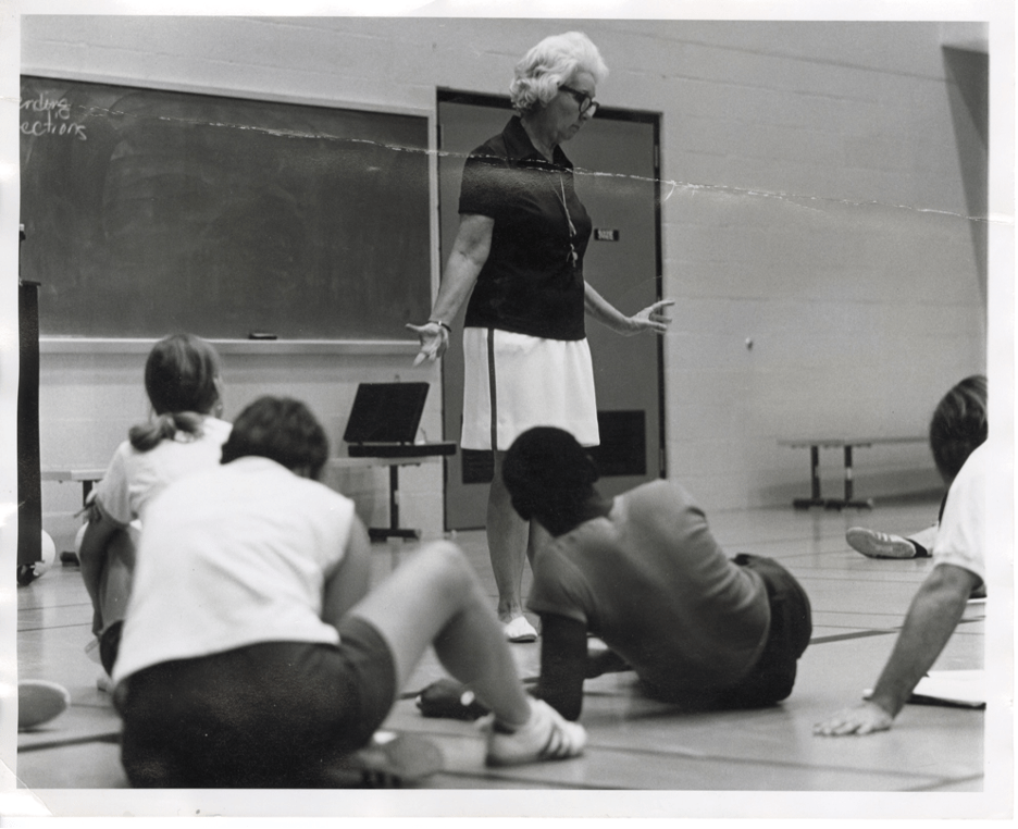 A photograph of Dr. Mary Evelyn Buice Alderson as she stands in front of a class seated on a gymnasium floor. She is teaching or lecturing.