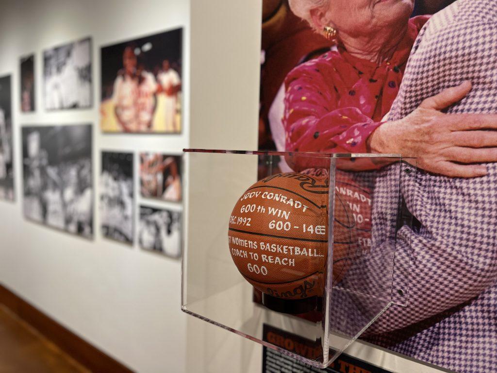 A photo of the Jody Conradt exhibit where a basketball commemorating her 600th career win is on display in a wall vitrine.