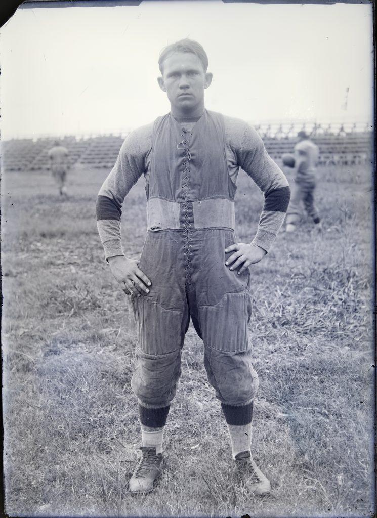 1913 image of football star Pete Edmond in his uniform with hands on hips on the football field posing, his freshman year.