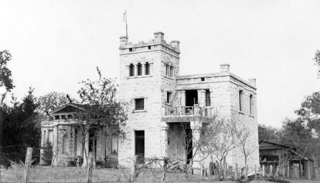 A black and white photo of the Elisabet Ney Museum in Austin Texas, a home built of white stone that resembles a very small castle.