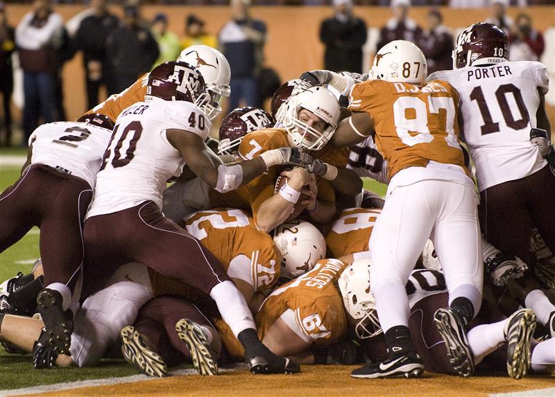 A color photo of a UT football player pushing into a pile and fighting to cross the goal line against a Texas A&M defense.