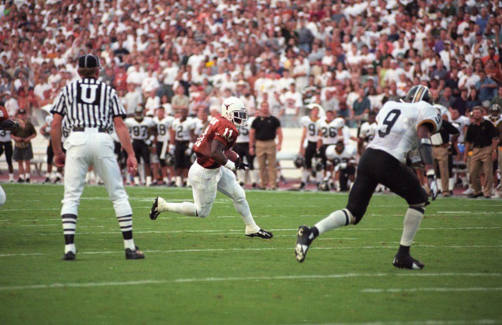 A color photo of Ricky Williams rushing with the football on the grass field at Texas Memorial Stadium