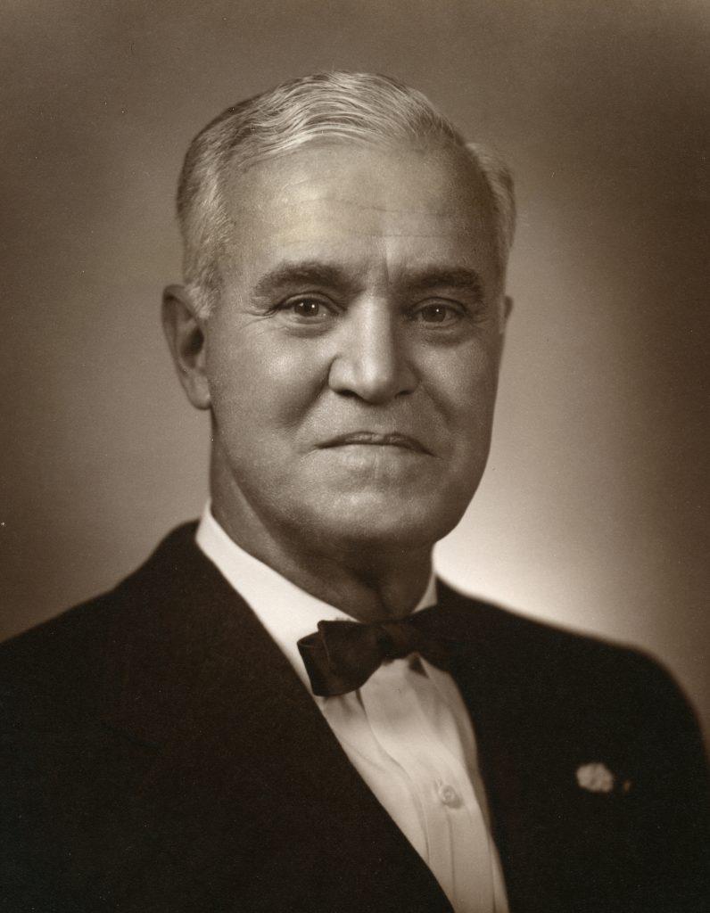 A black and white photo of L. Theo Bellmont in a bow tie and suit. He is clean shaven and his hair is light gray in color.