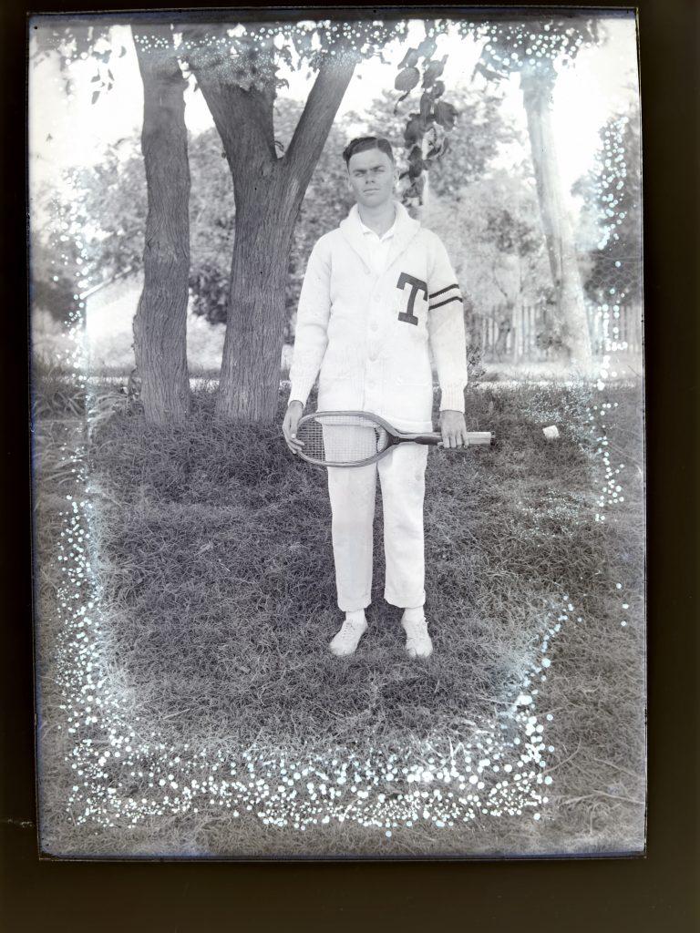 An image of 1914 men's tennis player Gillespie Stacy in his letterman's sweater and holding a tennis racket.