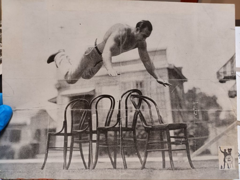 Black and white photograph of Bonomo jumping over chairs. The yellow residue along the sides has been removed.