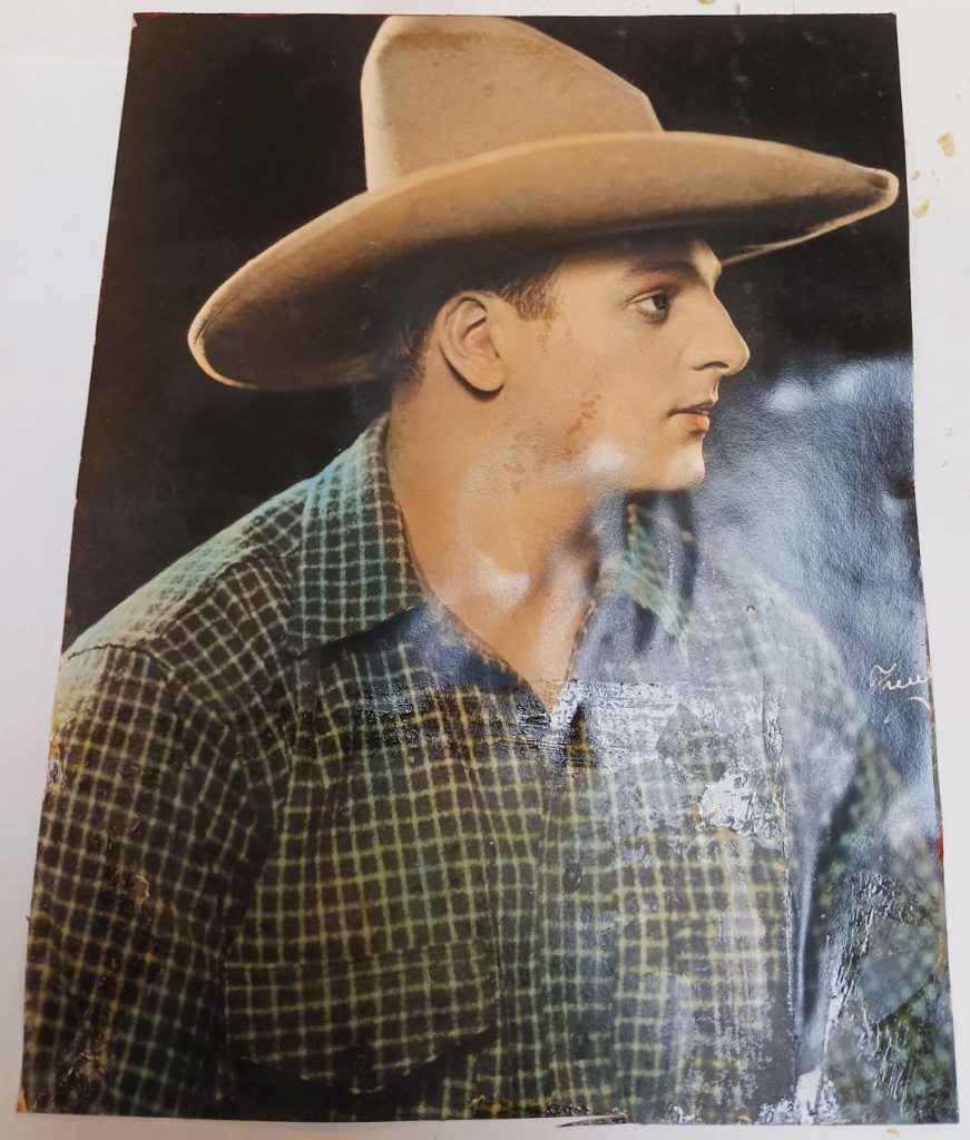 Colored photograph of Bonomo in plaid shirt and cowboy hat. The construction paper and other photograph fragment once stuck to the front have been removed.