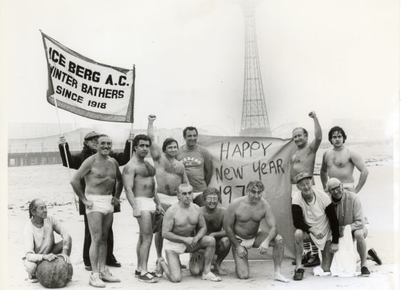 Vic Boff and Iceberg Athletic Club on beach with "Happy New Year" banner.