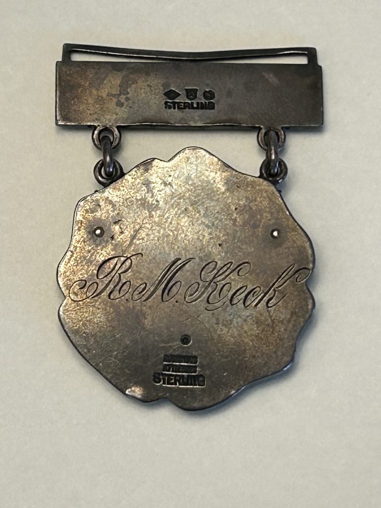 The backside of a silver medal, with script text reading "Ray M. Keck."