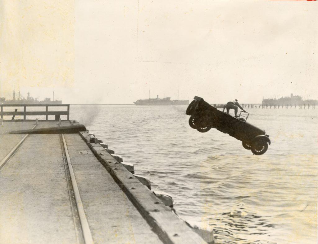 Joe Bonomo riding on top of car as car flies off pier towards the water. 