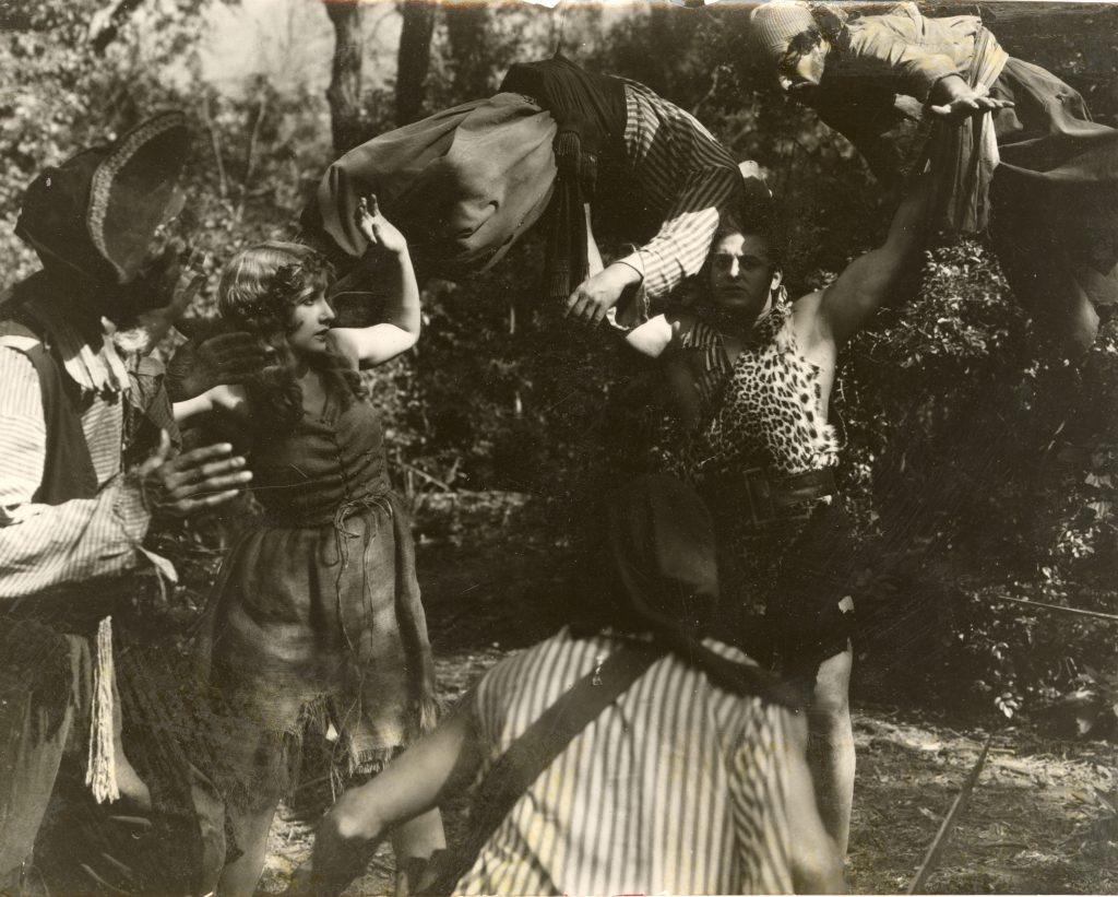 Joe Bonomo holding two men over his head, one in each hand, while woman and two men look on.