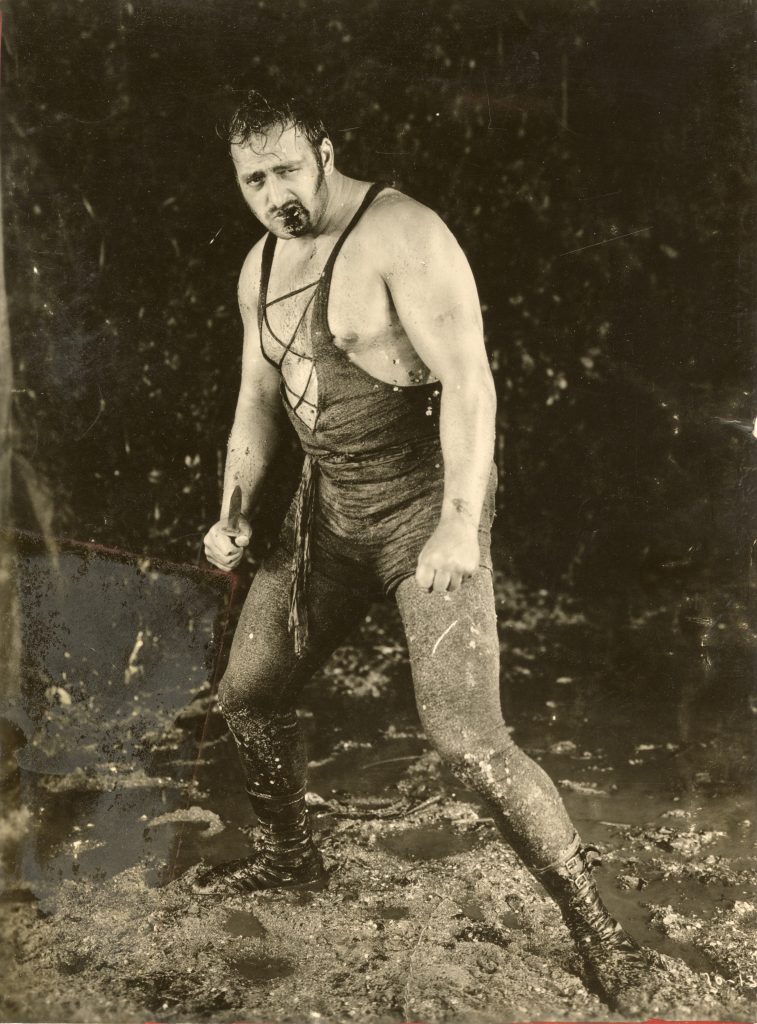 Portrait of Joe Bonomo standing with bloodied mouth and knife in his hand.