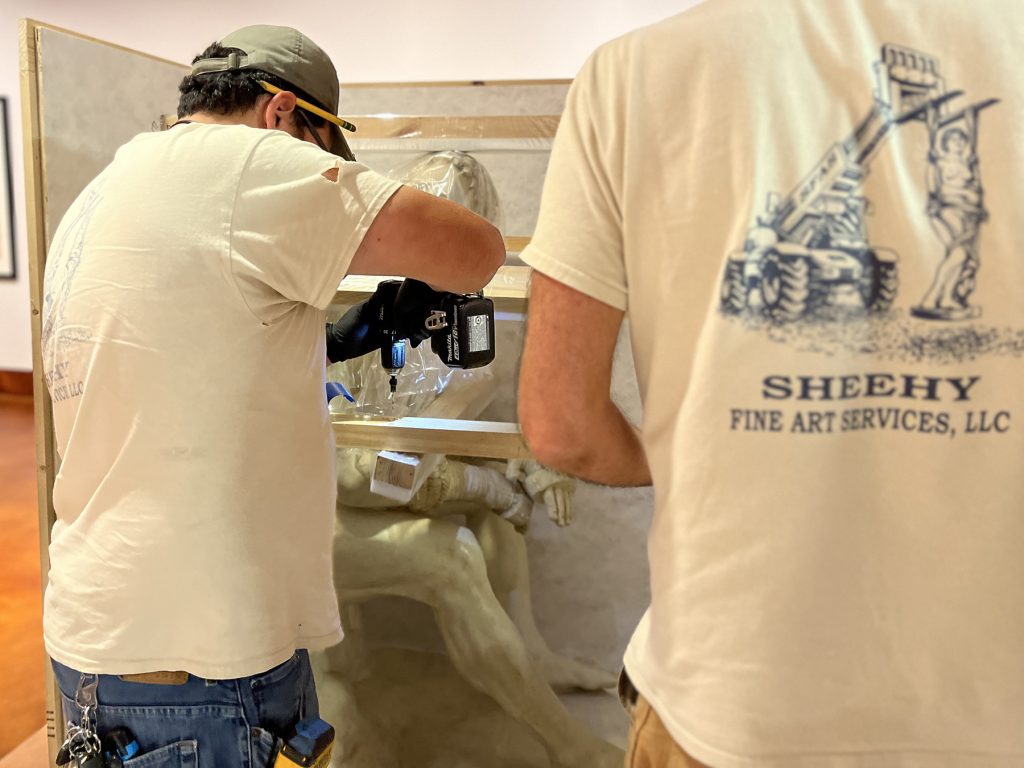 A man installs a brace within the crate of The Seated Boxer to ensure stability and safety during transit.