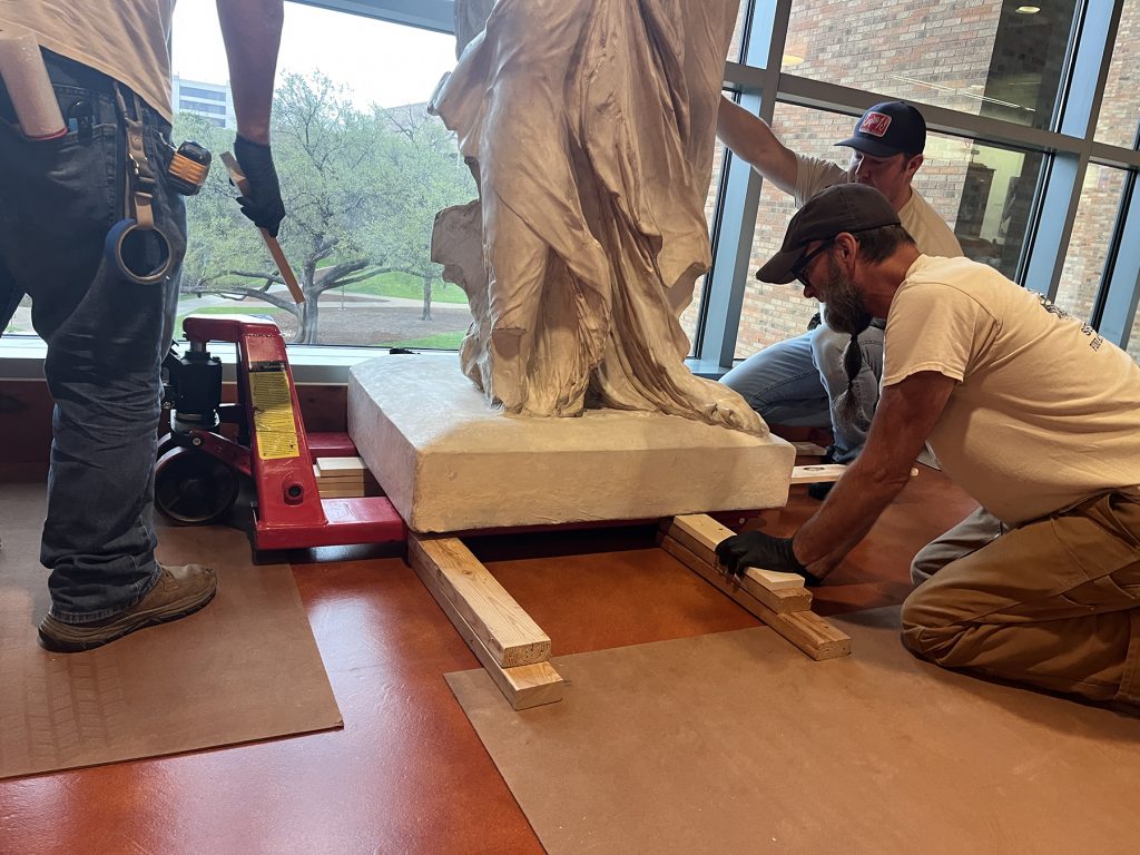 The base of Winged Victory being lowered from a pallet jack. Step one: transitioning from jack to wood boards.