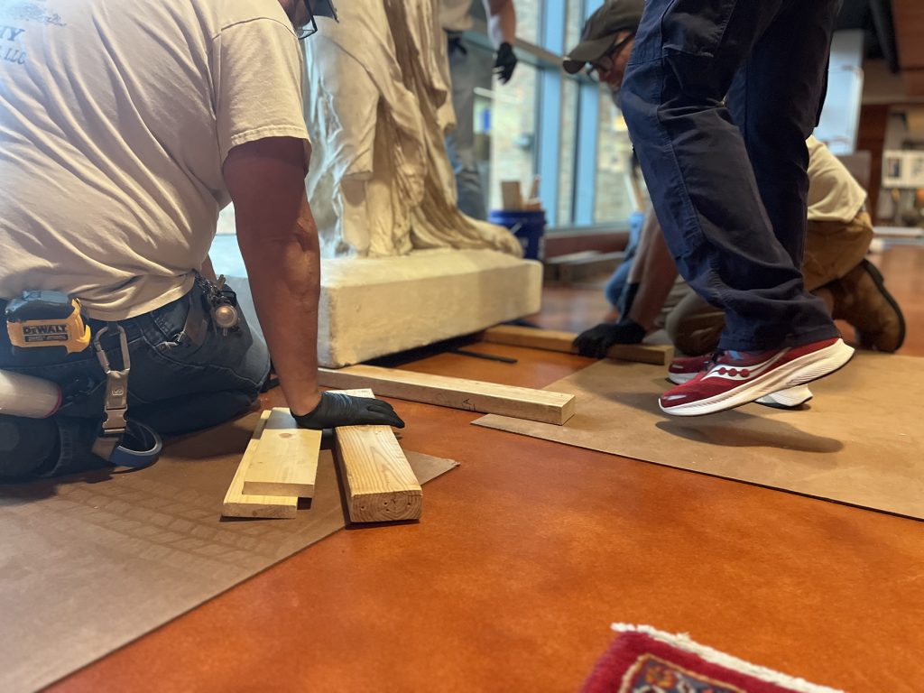 Step three in lowering the base of Winged Victory. The base sits on just one set of one by fours and the crew begins to place a specialized material to buffer between the cast and the Stark Center's specialized floor.