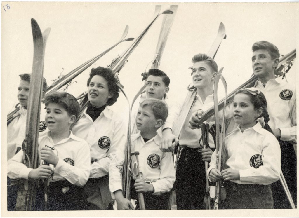 Bonnie standing with children, all holding skis and wearing Addlepate Ski School badges. 