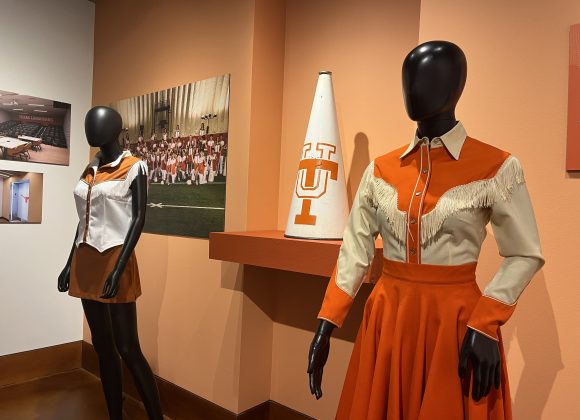 A close up photo of a 1961 female cheer uniform from the University of Texas with a megaphone behind. In the background a contemporary female uniform from 2026.