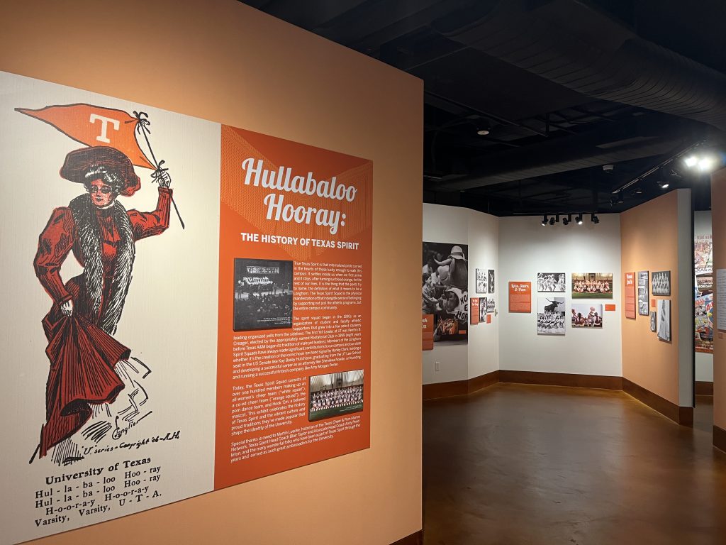 A color photograph of the entrance to the new exhibit, especially in focus is an illustration of a woman cheering for Texas from the late 1800s or early 1900s.